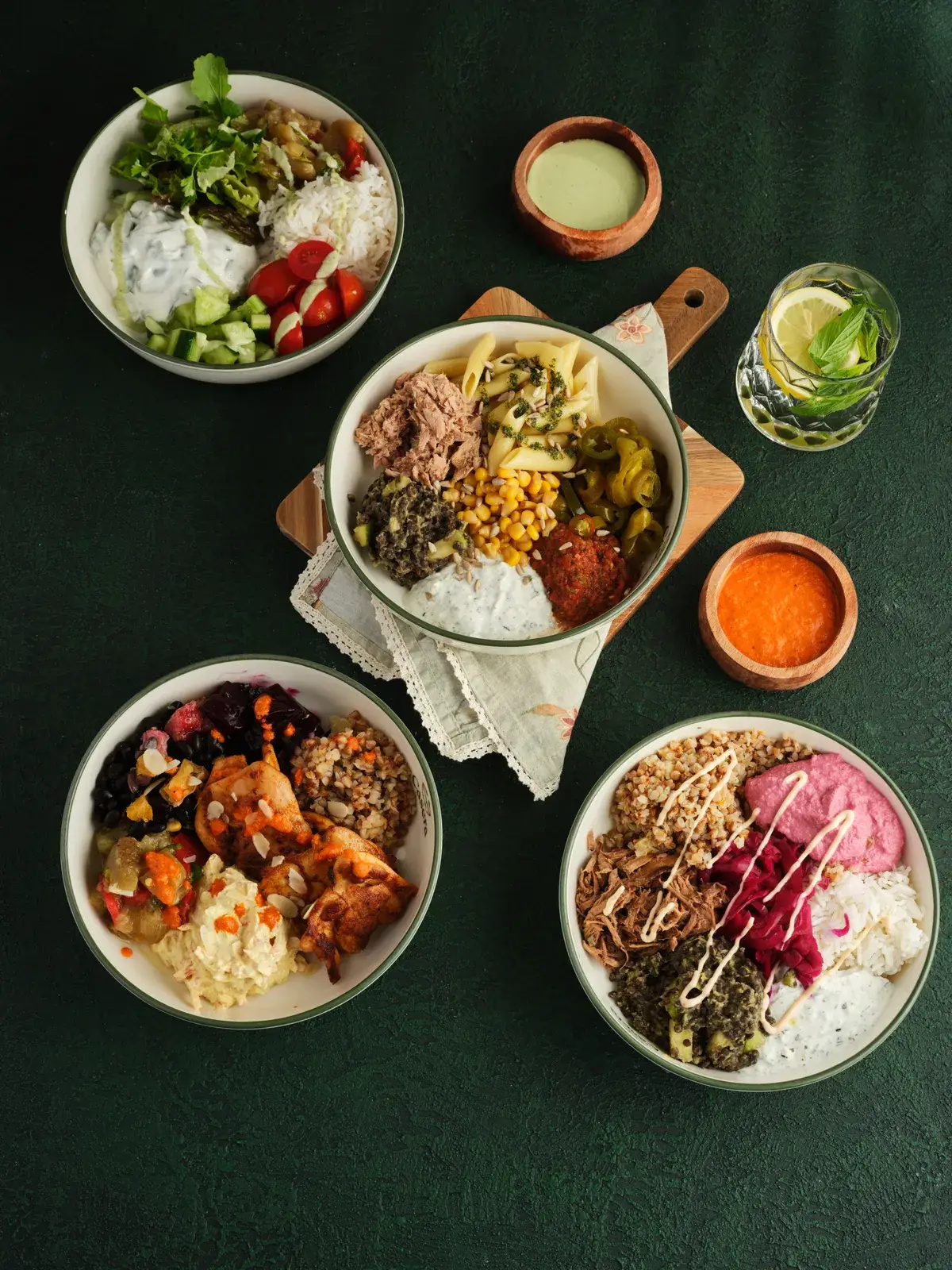 Koyu yeşil masa üzerinde dört farklı Casera bowl'u, soslar ve limonata